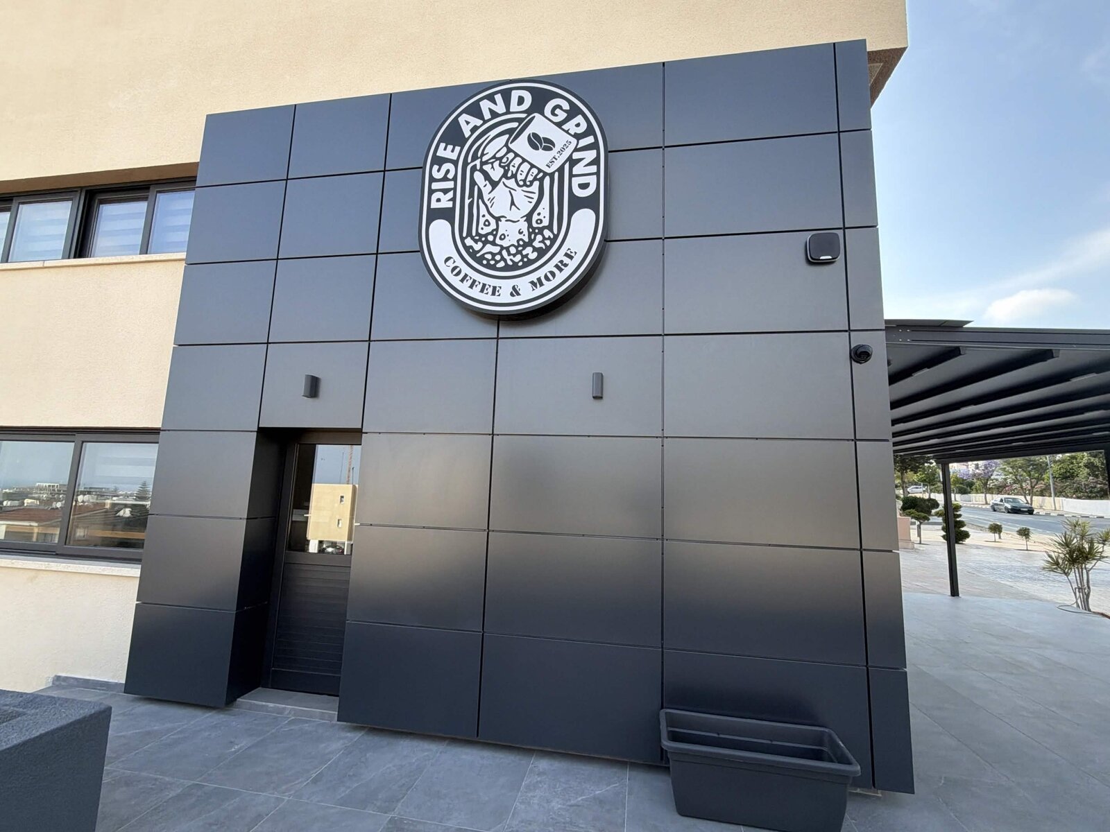 Rise & Grind coffee shop logo badge on the building facade in Paphos